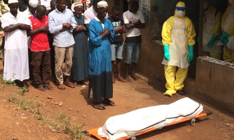 Mourners pray before the body of a suspected Ebola victim is taken away for burial