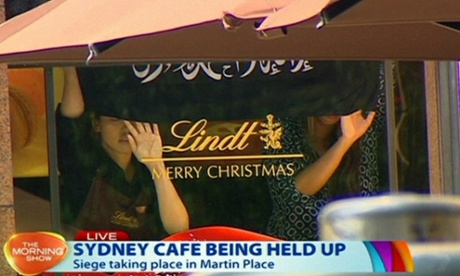 This image taken from video shows people holding up what appeared to be a black flag with white Arabic writing on it, inside a cafe in Sydney, Australia Monday, Dec. 15, 2014. A hostage siege in Sydney that began Monday morning and ended with a police raid 16 hours later unfolded before the world on Monday. (AP Photo/Channel 7 via AP Video) AUSTRALIA OUT