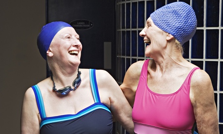 Two older women in swimsuits and swim caps laughing