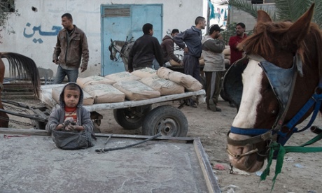 Nine-year-old Adham scrapes up concrete dust into his bag to sell as men haggle in the background over the price of a cart of black-market concrete.
