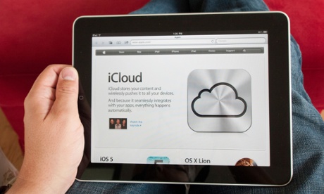 A man holds in his lap an iPad displaying the iCloud page on Apple's website. 