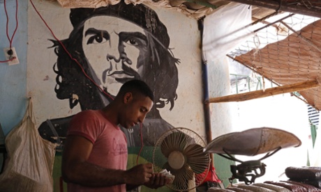 A worker who sells beans counts money at a state-run market stall decorated with a mural of Cuban revolutionary hero Ernesto 