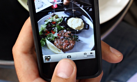 A man takes a picture with his mobile of food on his plate.