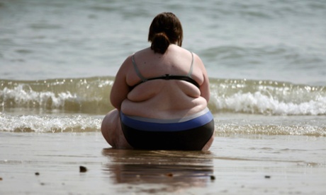 Very large woman sits by the sea
