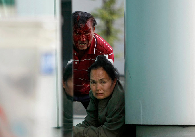 Bangkok Gunfight: An injured Thai man and a woman peer around a wall in Bangkok