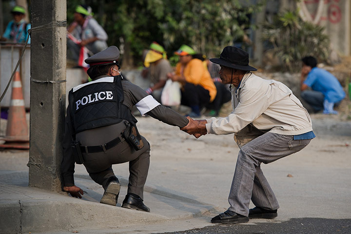 Bangkok Gunfight: A man helps a police officer to take cover in Bangkok