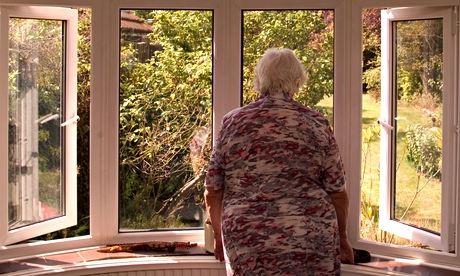An elderly woman looking out of her front room window