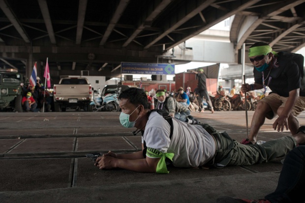 An anti-government protester takes cover after shooting his gun during clashes in Bangkok on the eve of tense Thai elections.