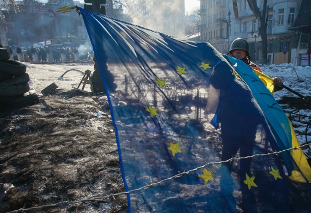 An anti-government protester hangs Ukrainian and EU flags on a barricade that faces a cordon of riot police in Kiev.