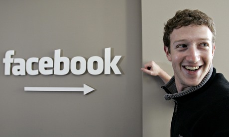 Mark Zuckerberg CEO of Facebook stands next to a Facebook sign smiling