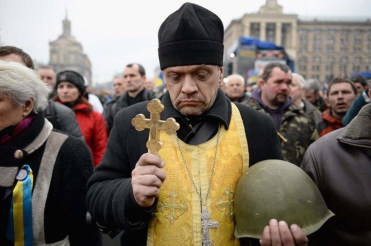 Kiev protests: A priest holds the helmet of a demonstrator killed in clashes