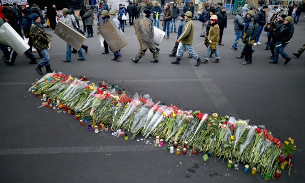 Men carrying shields and batons pass flowers in Independence Square, where dozens of protestors were killed in clashes with riot police last week in Kiev, Ukraine.