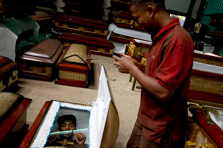 Caracas : A worker takes a picture of a fellow worker inside a coffin at a caskets fa