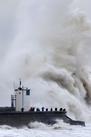 People look on as waves break over the harbour wall at Porthcawl in Wales.