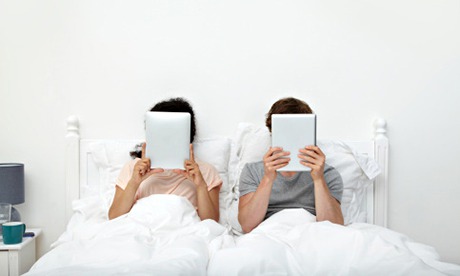 Couple looking at digital tablets in bed