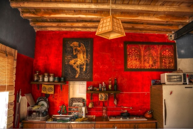 a photo of a kitchen with red walls, a painting of an angel, a wooden lampshade sink, fridge and drying rack
