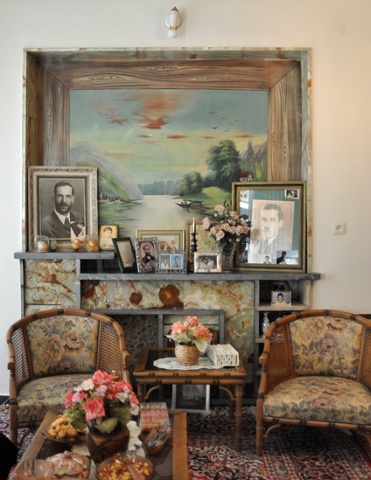 a landscape painting, framed photos and two wooden chairs in a living room