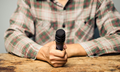 Young man is sitting at an old wooden table with a microphone in his hand