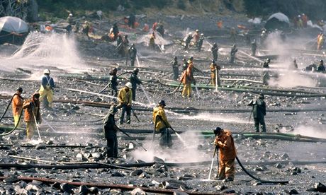 Workers in protective suits use pressure washers to clean oil from a beach after the 1989 spill
