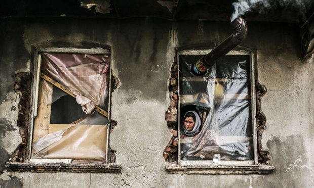 A Syrian refugee woman looks out from a window with no glass, in a house in the Kucukpazar area of Istanbul, Turkey.