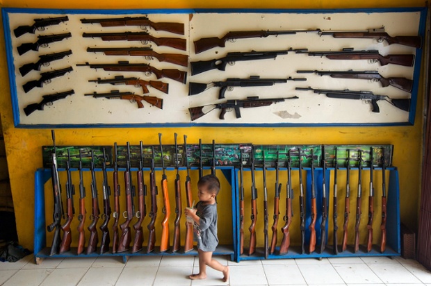 The son of the owner walks past air rifles on display at the shop in Cipacing, Indonesia.  The small village is known for its gunsmiths make thousands of air rifles annually with most of them made in small back garden operations.