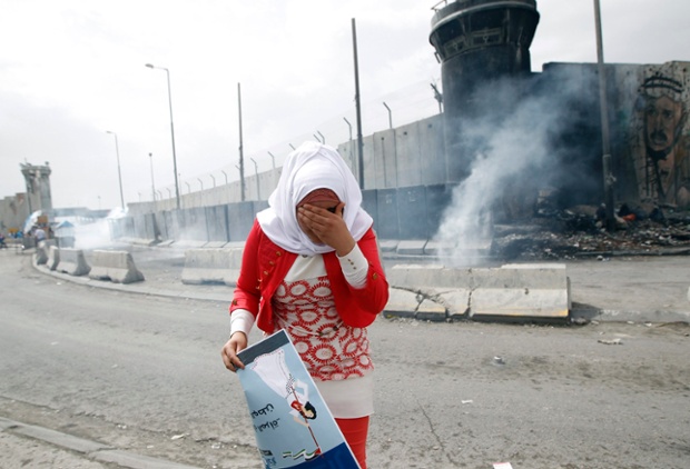 A Palestinian woman walks away from tear gas during clashes with Israeli security forces, after a rally marking International Women's Day at Qalandiya checkpoint near the West Bank city of Ramallah