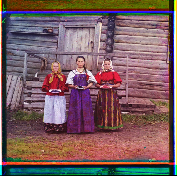 Three young women offer berries to visitors to their izba, a traditional wooden house, in a rural area along the Sheksna River, near the town of Kirillov, circa 1909.