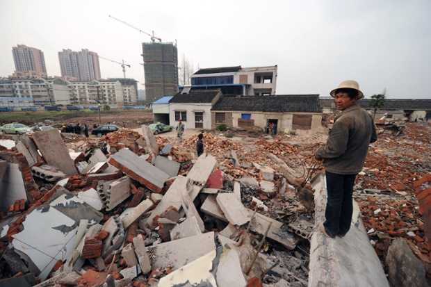 A worker looks out over rubble to 75-year-old Yao Baohua's house
