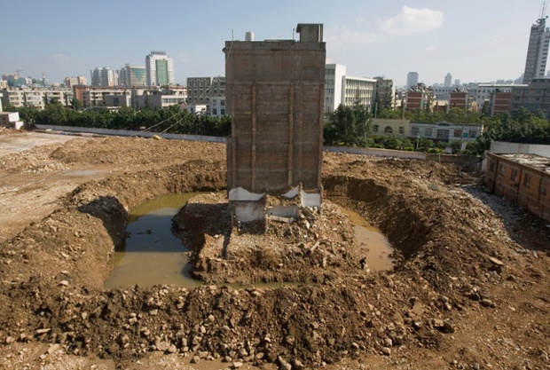 October 2010: Owner Zhao Xing, 58, collects water near his partially demolished nail house, at a construction site in Kunming, Yunnan province. Water and electricity supplies to his house have been cut.