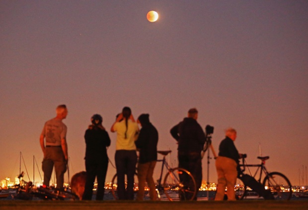 People watch as the blood moon rises over the water in Williamstown, Melbourne, Australia.