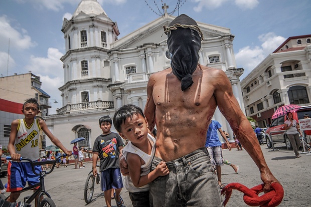 A hooded penitent carries his son outside the cathedral in San Fernando town, Philippines.