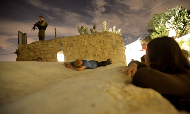 An Israeli soldier stands guard as an Ultra-Orthodox Jews lays on the tomb Kifl Hareth, West Bank.