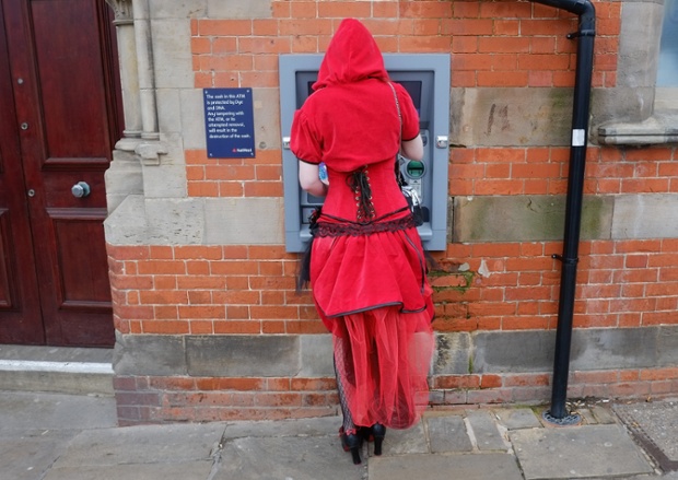 A woman dressed a Little Red Riding Hood withdraws money from a cashpoint. ~ Getty Photograph by Ian Forsyth