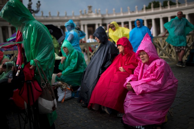 People wearing raincoats sit in St Peter's Square as pilgrims and faithful gather in Rome for the ceremony at the Vatican.