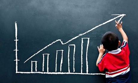 A boy aged about six in a red top chalks up a sales report on a blackboard