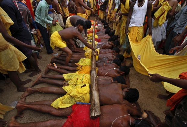 A man breaks coconuts on a wooden pole placed on the backs of villagers lying on hot sand, at the annual Danda festival or the festival of self punishment in India.