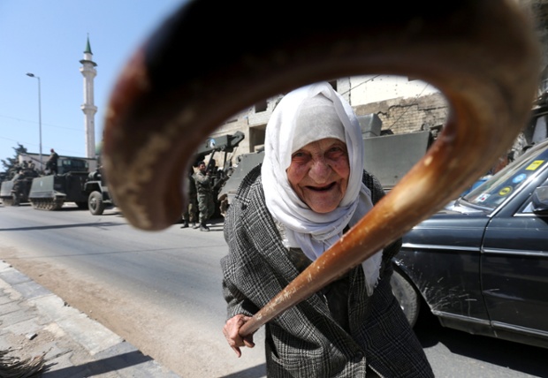 An elderly Lebanese woman gestures with her cane as she crosses the street in front of army armoured personnel carriers in Tripoli , Lebanon.