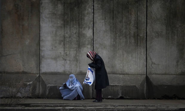 A woman stops to give money to a beggar wearing a burqa outside a police station in Kabul.