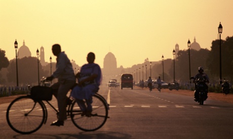 A couple on a bicycle pedal past the Capital building in New Delhi India at sunset