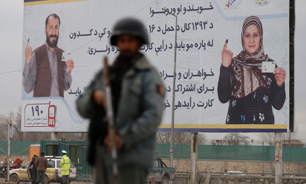 A policeman stands near a billboard for the presidential election at a checkpoint in Kabul