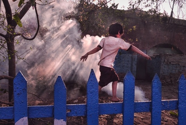 'A child runs past a railway quarter near the Sealdah railway station at Kolkata while smoke rises in his background through a canopy of hedges and trees.'