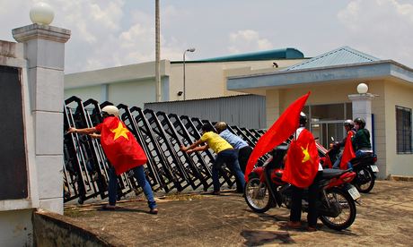 Protesters holding Vietnamese flags attempt to push down the gate of a factory in Bien Hoa