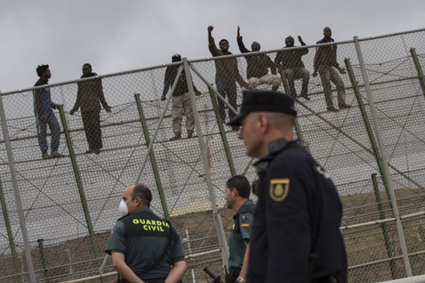 Melilla, Spain: Police stand guard as migrants sitting on a fence while attempting to enter the Spanish enclave from Morocco.