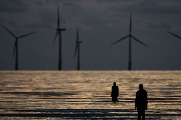 Figures from Antony Gormley's art installation Another Place in front of the turbines of the Burbo Bank offshore windfarm in the mouth of the river Mersey