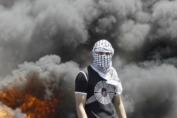 A Palestinian protester stands in front of burning tyres during clashes with Israeli security forces following a weekly demonstration against the expropriation of Palestinian land by Israel in the West Bank village of Kfar Qaddum, near Nablus.
