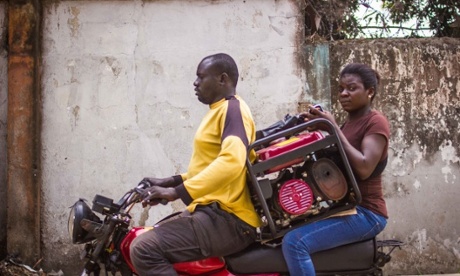 A woman carrying a small generator on an Okada (motorcycle taxi).