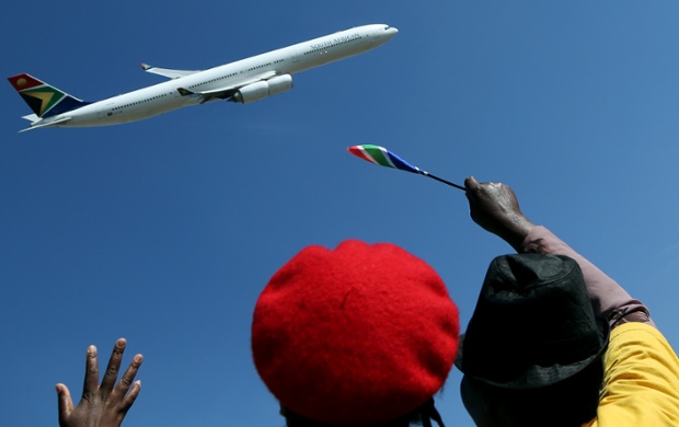 Ruling party supporters wave as a South African Airways Airbus flies past during the inauguration of the Union Building in Pretoria, South Africa.