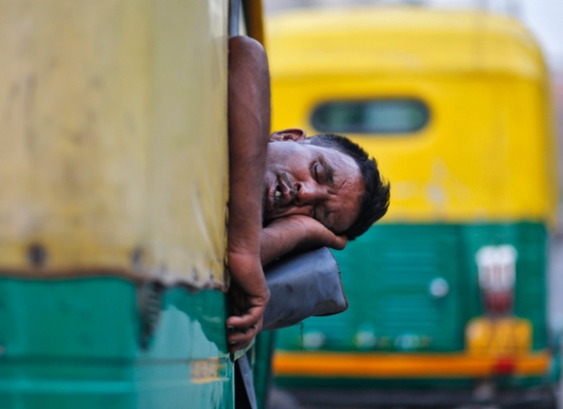 A driver takes a nap inside his parked auto-rickshaw along the roadside in the old quarters of Delhi, India.