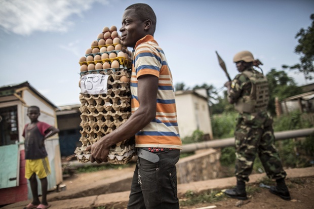 A vendor carries a rack of eggs for sale past a Rwandan soldier from the African-led International Support Mission to the Central African Republic (MISCA) contingent patrolling the streets in the Christian Miskine district in Bangui,.