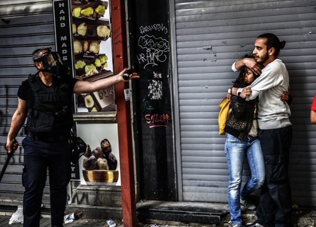 Istanbul, Turkey: A man protects a woman as they face a police officer dispersing protesters who gathered during the one year anniversary of the Gezi park and Taksim square demonstrations.